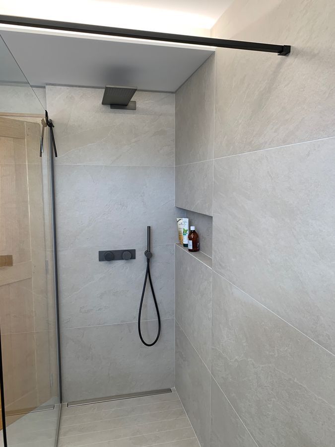 Une salle de bain avec une douche à l'italienne et un pommeau de douche noir.