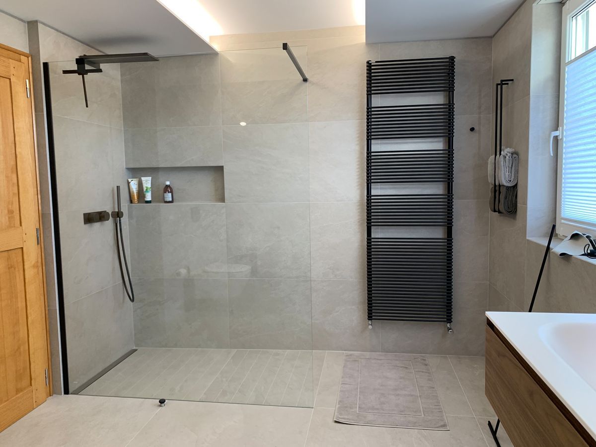 Salle de bain moderne avec douche à l'italienne, carrelage gris, sèche-serviettes et porte en bois.