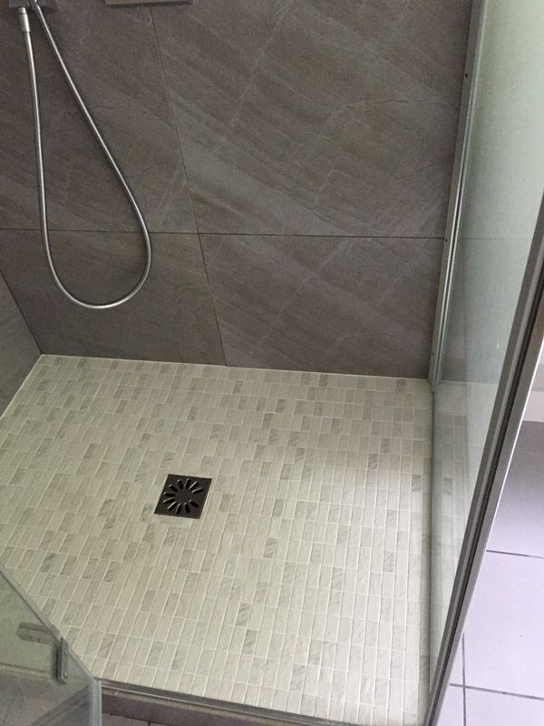 Une cabine de douche avec un drain et une pomme de douche dans une salle de bain.