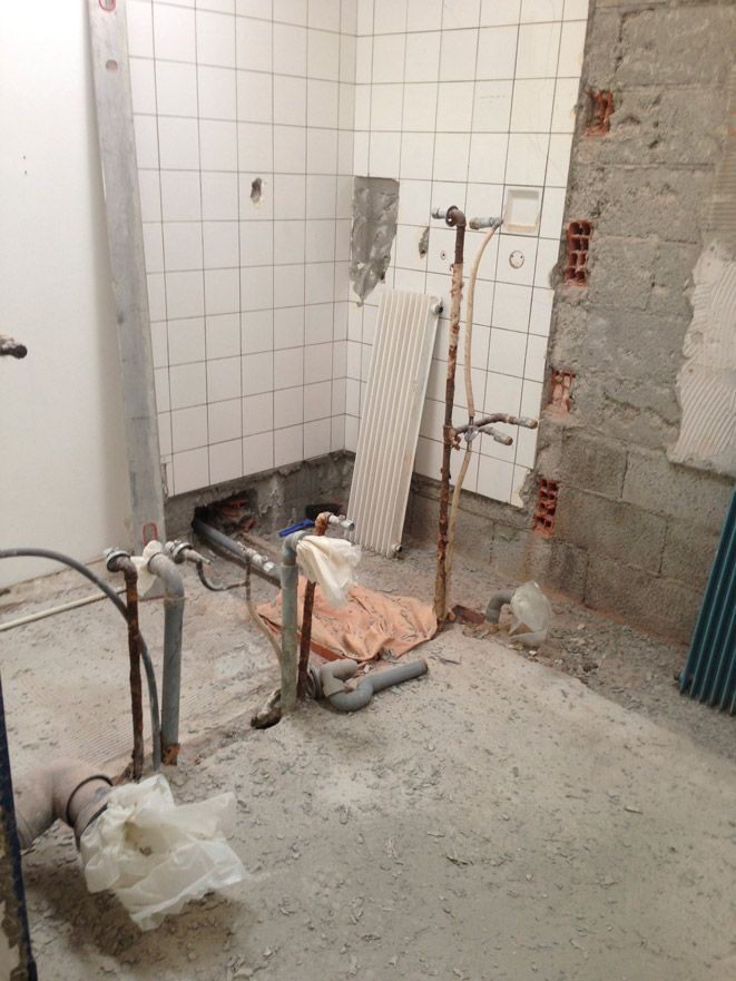 Une salle de bain en construction avec carrelage et tuyaux blancs.