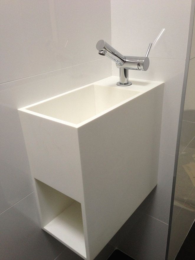 Évier blanc rectangulaire avec rangement ouvert en dessous, robinet chromé, monté sur mur blanc.