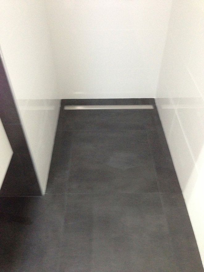 Une salle de bain avec un sol carrelé noir et des murs blancs.