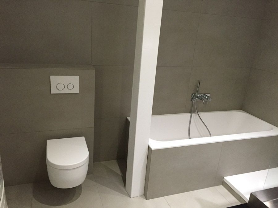 Salle de bain moderne avec murs en carrelage gris, toilettes blanches et baignoire.
