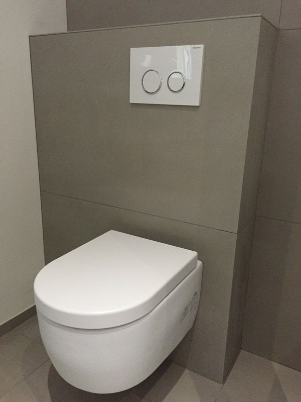 Une toilette blanche est fixée au mur dans une salle de bain