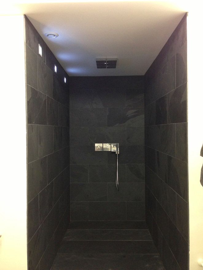 Cabine de douche carrelée foncée avec pommes de douche suspendues et murales et plafonniers encastrés.