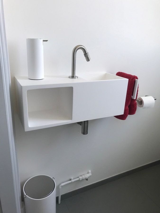 Une salle de bain avec un lavabo, du papier toilette, un distributeur de savon et une poubelle.