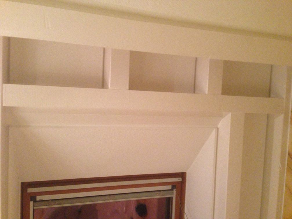 Une cheminée blanche avec un cadre et des étagères en bois