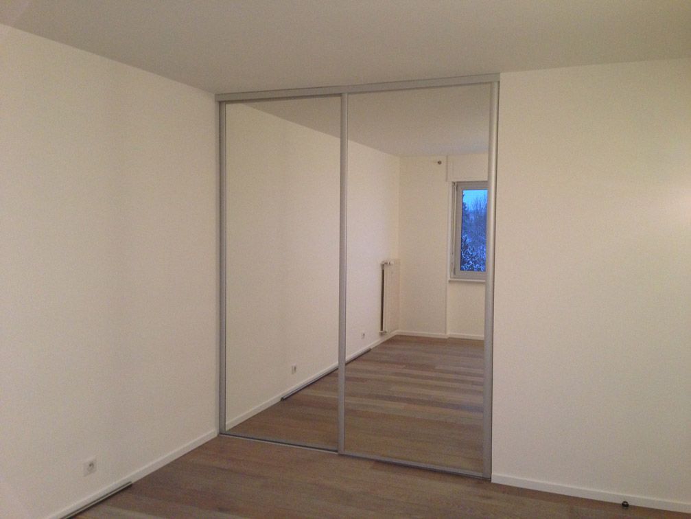 Une chambre avec portes coulissantes en miroir et une fenêtre.