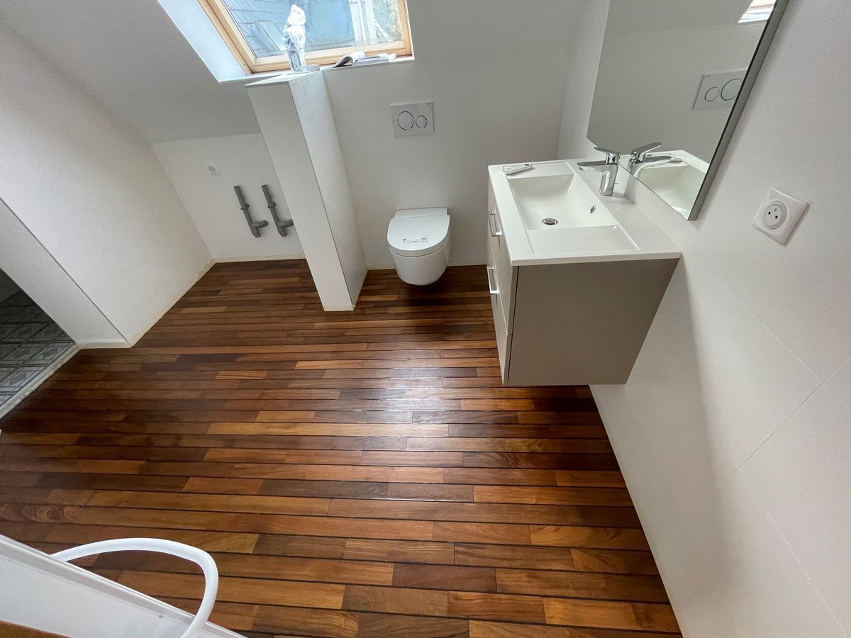 Une salle de bain avec parquet, lavabo, WC et miroir.