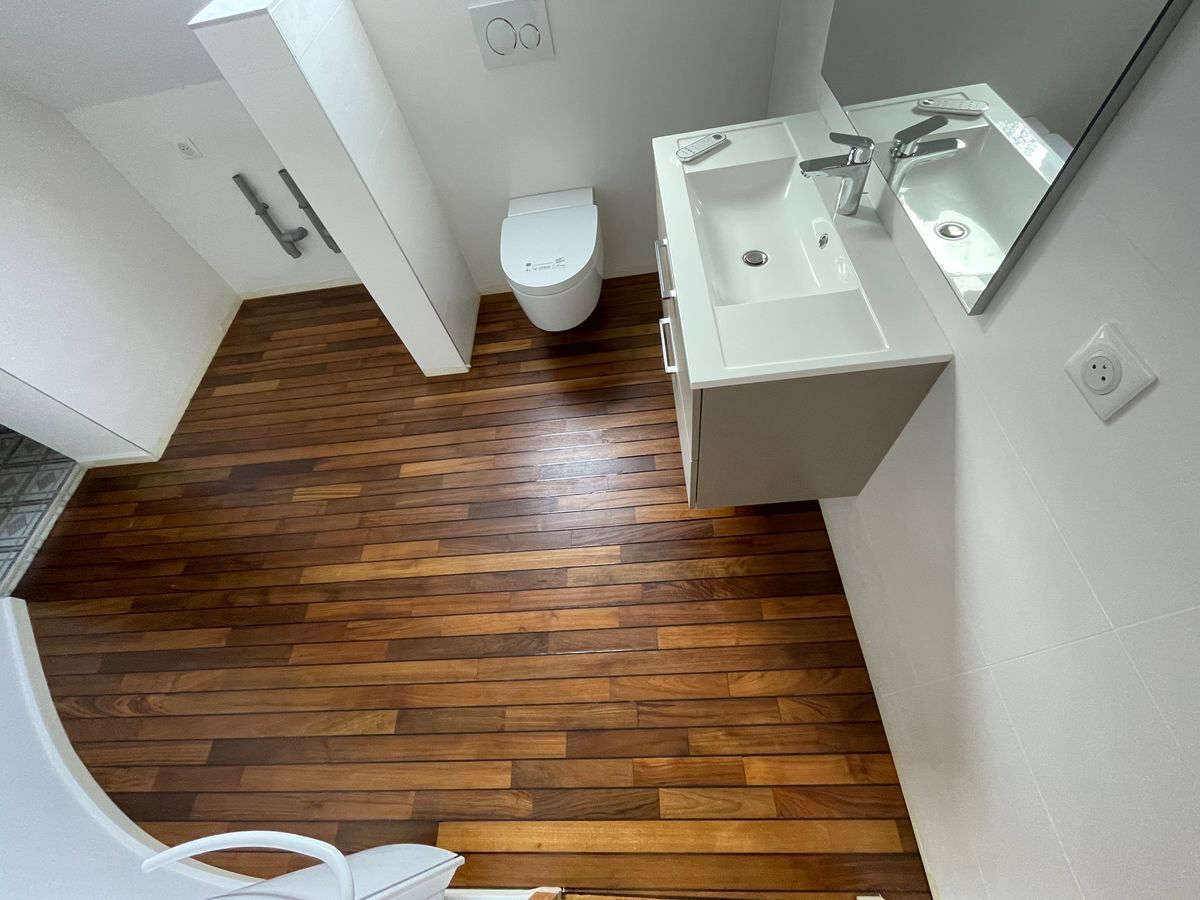Une salle de bain avec WC, lavabo, miroir et parquet.