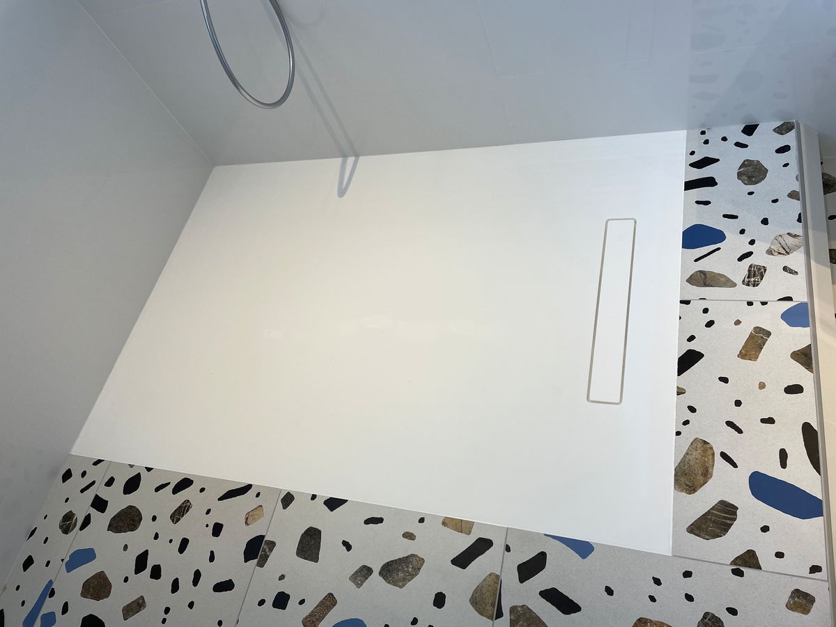 Un receveur de douche blanc avec un drain au sol dans une salle de bain.