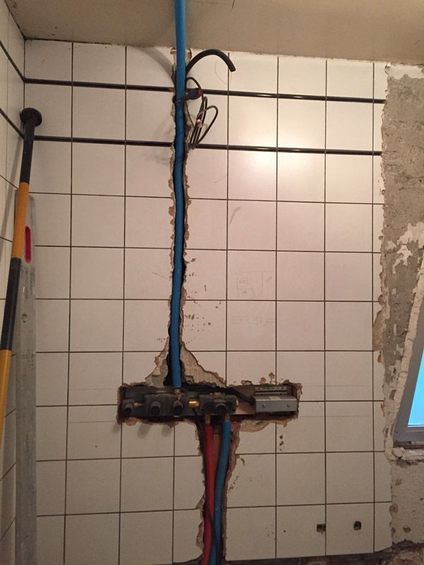 Une salle de bain avec du carrelage blanc et une pomme de douche cassée