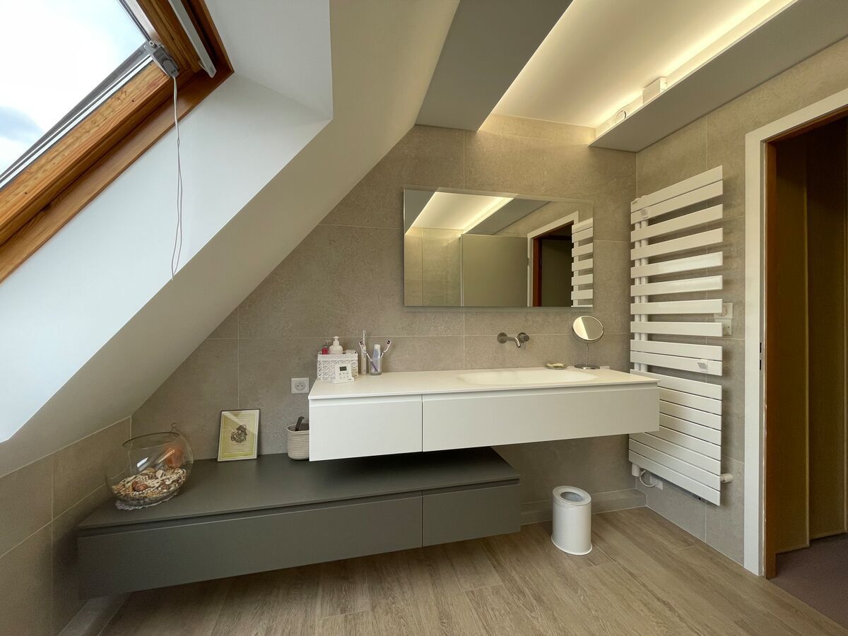Salle de bain moderne avec plafond en pente, vanité et porte-serviettes chauffant blanc.