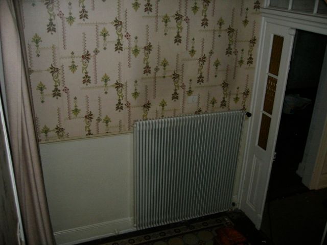 Une pièce avec un radiateur et du papier peint au mur.