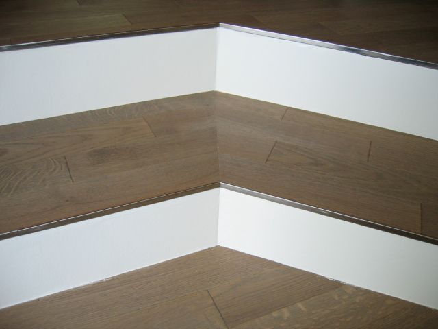 Un coin d'un plancher en bois avec des garnitures blanches