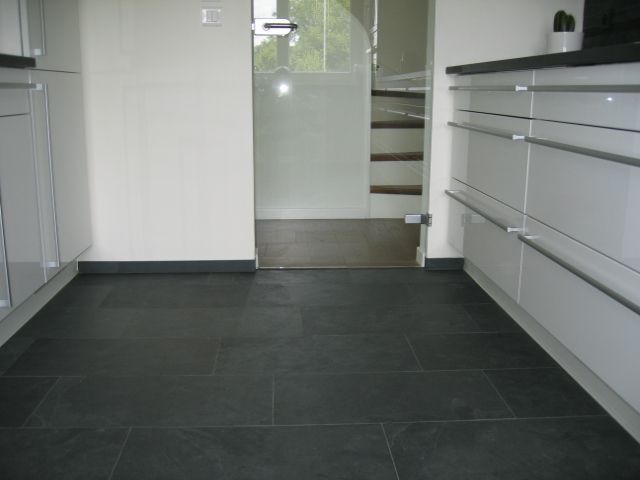 Une cuisine avec du carrelage noir et des armoires blanches