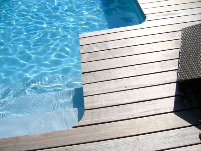Une terrasse en bois avec une piscine en arrière-plan
