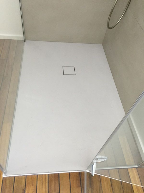 Une cabine de douche avec un drain carré et un plancher en bois.