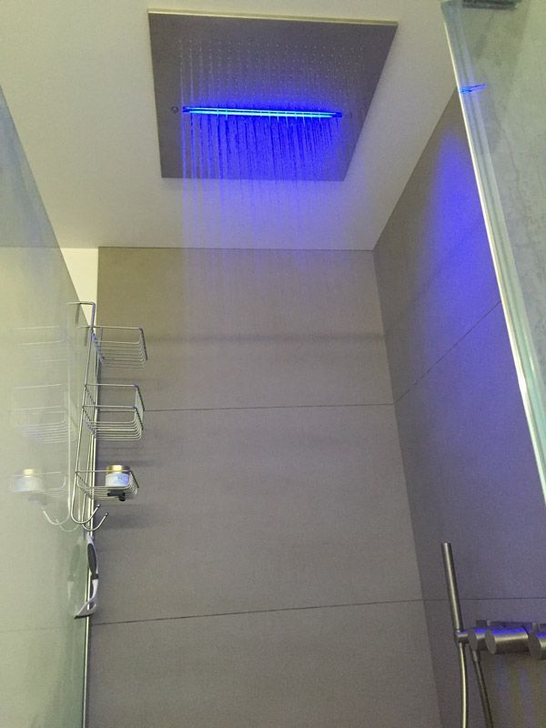 Une salle de bain avec une pomme de douche et une lumière bleue au plafond.