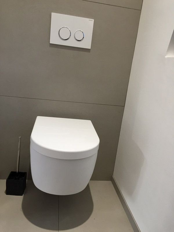 Une toilette blanche est fixée au mur dans une salle de bain