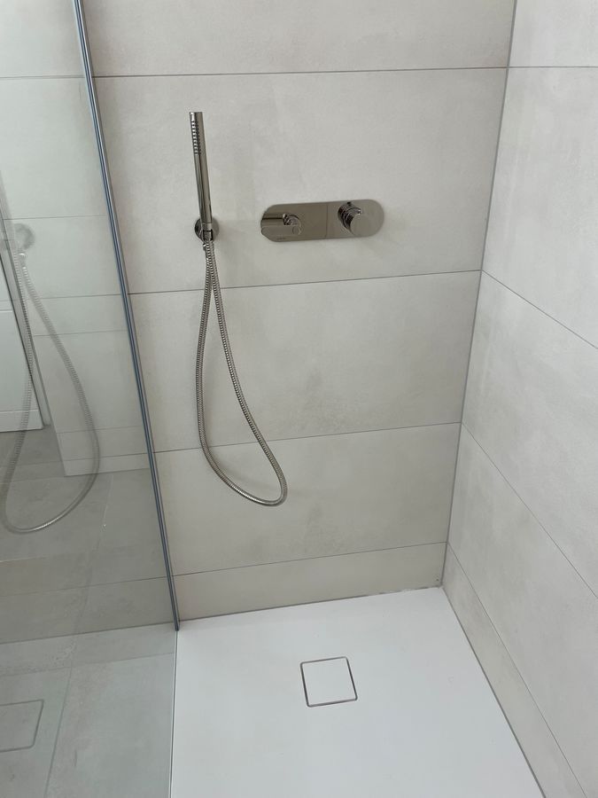 Une douche avec une pomme de douche et un drain carré