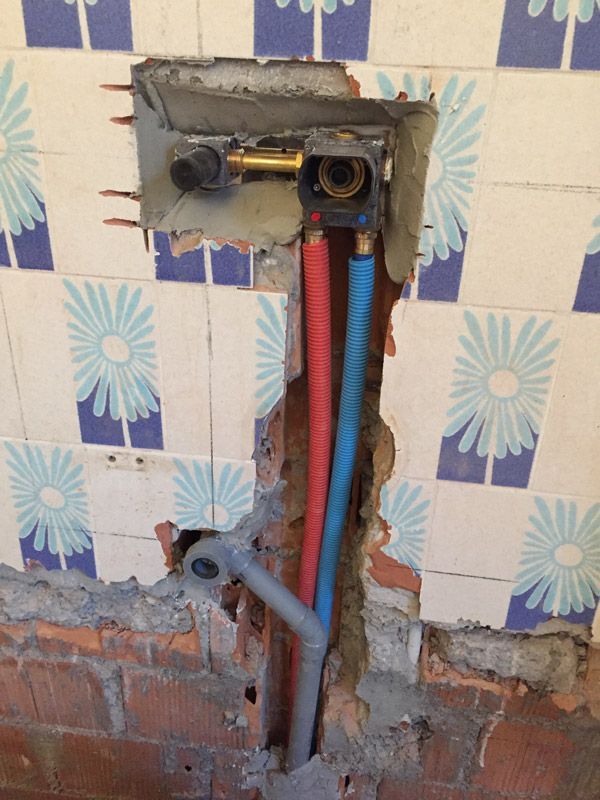 Un trou dans un mur avec un tuyau bleu et rouge qui en sort