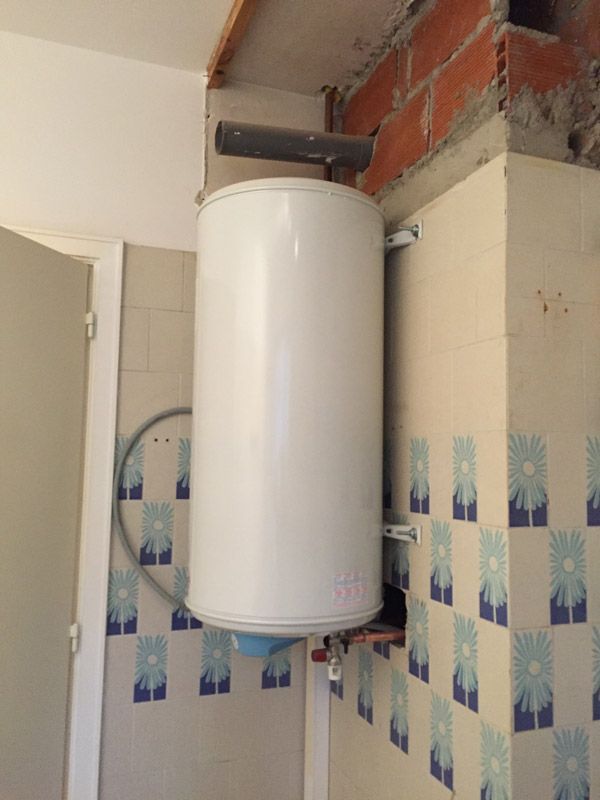 Un chauffe-eau blanc est accroché à un mur de briques dans une salle de bain.