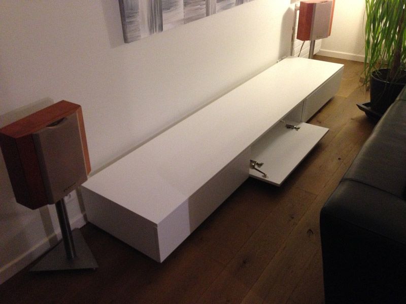 Un salon avec un long centre de divertissement blanc et deux haut-parleurs