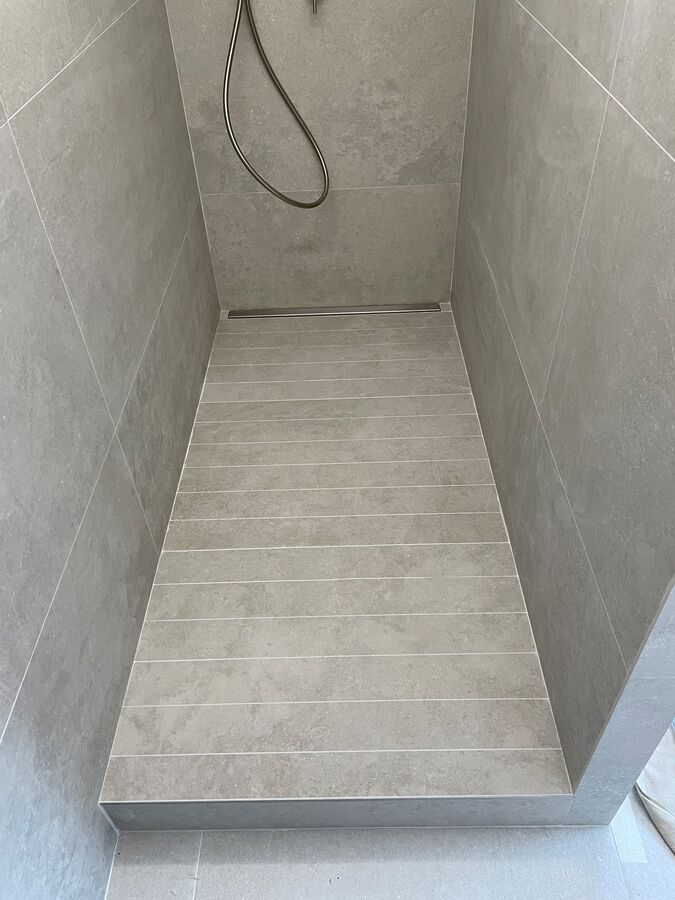 Une douche à l'italienne avec un sol carrelé et une pomme de douche.