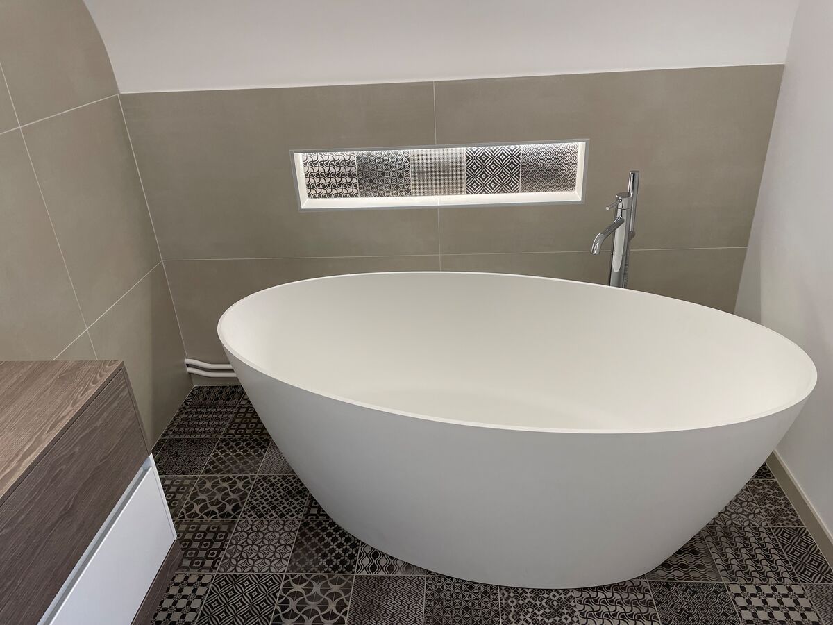 Une baignoire blanche est posée sur un sol carrelé dans une salle de bain.