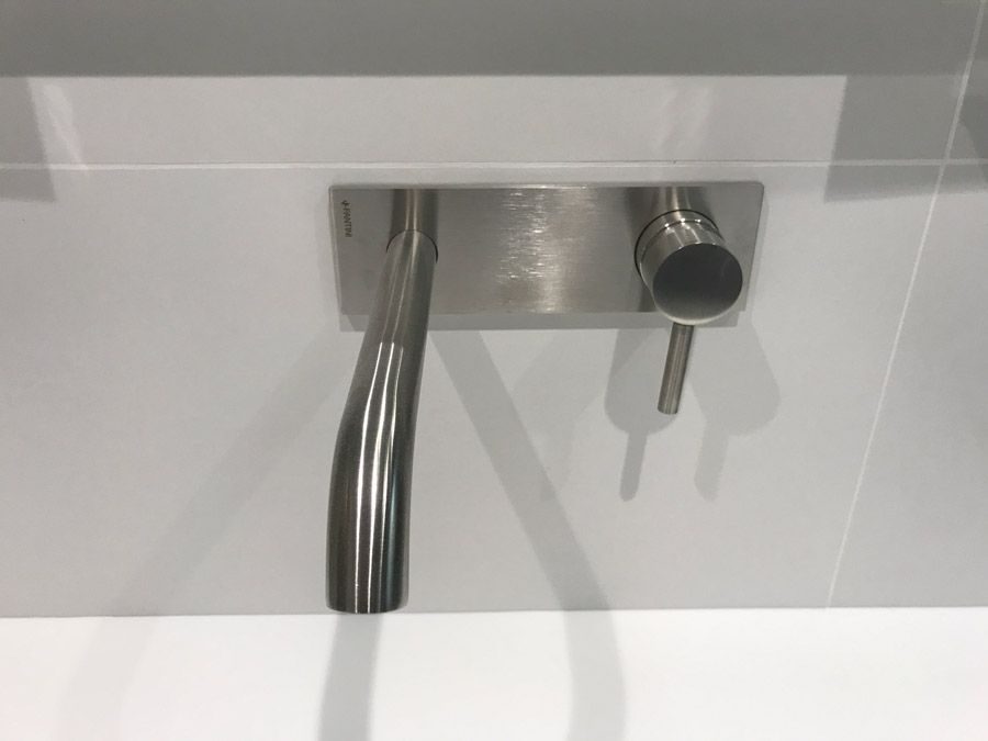 Un robinet de lavabo mural en acier inoxydable dans une salle de bain.