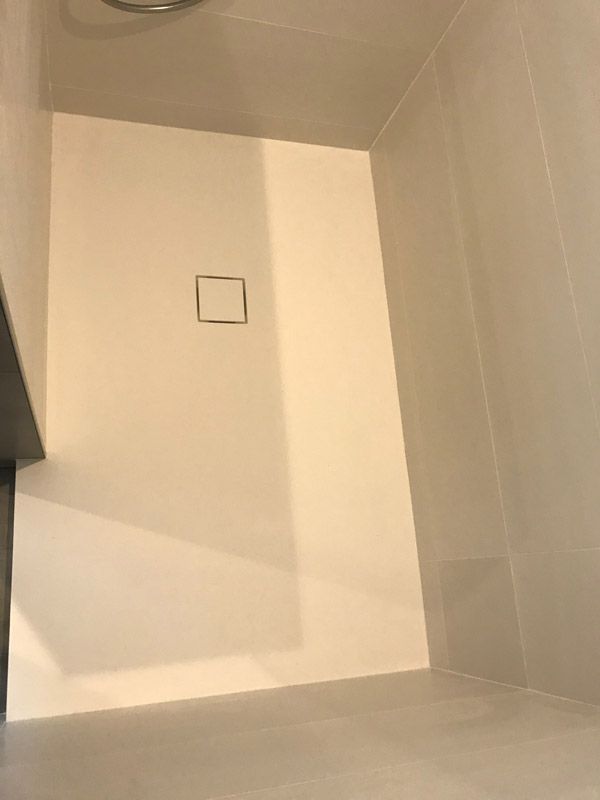 Une cabine de douche blanche dans une salle de bain avec un drain carré.