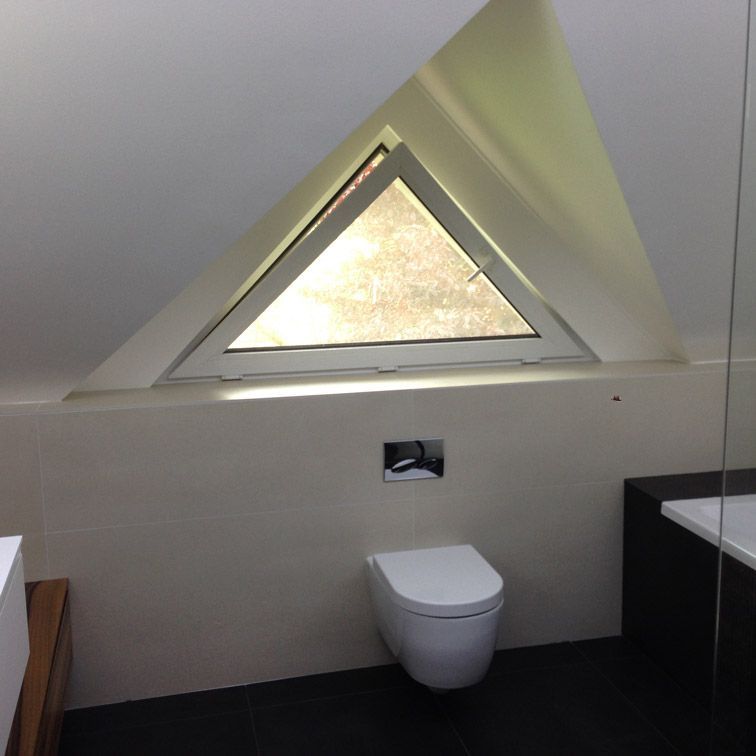 Une salle de bain avec une fenêtre triangulaire et des toilettes