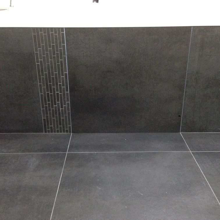 Une salle de bain avec du carrelage noir et un mur blanc