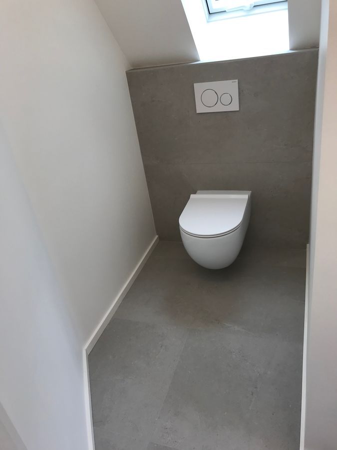 Une toilette est située dans une petite salle de bain sous une fenêtre.