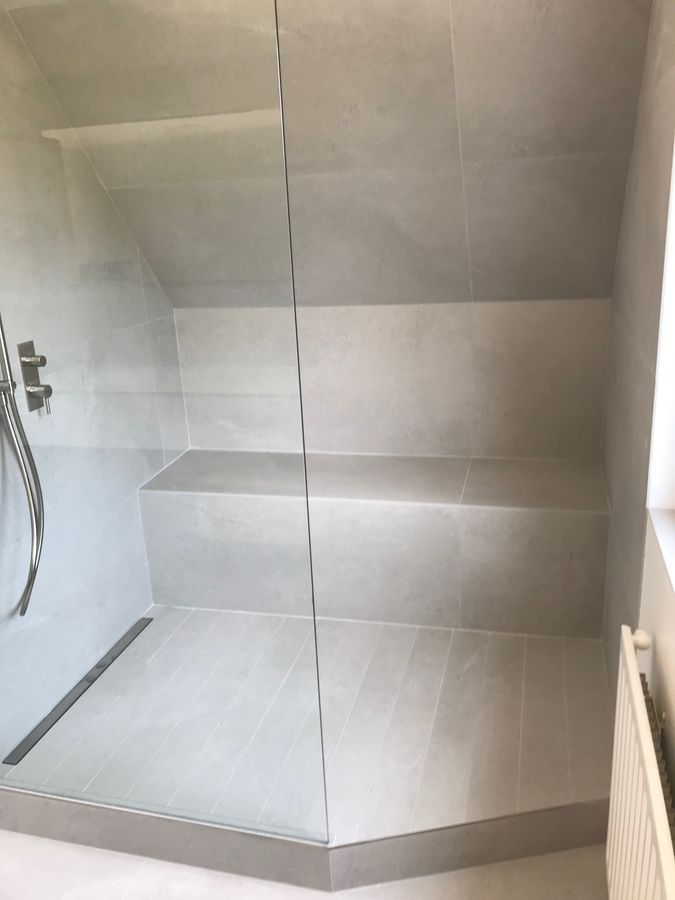 Une salle de bain avec une douche à l'italienne avec une porte vitrée et un banc.