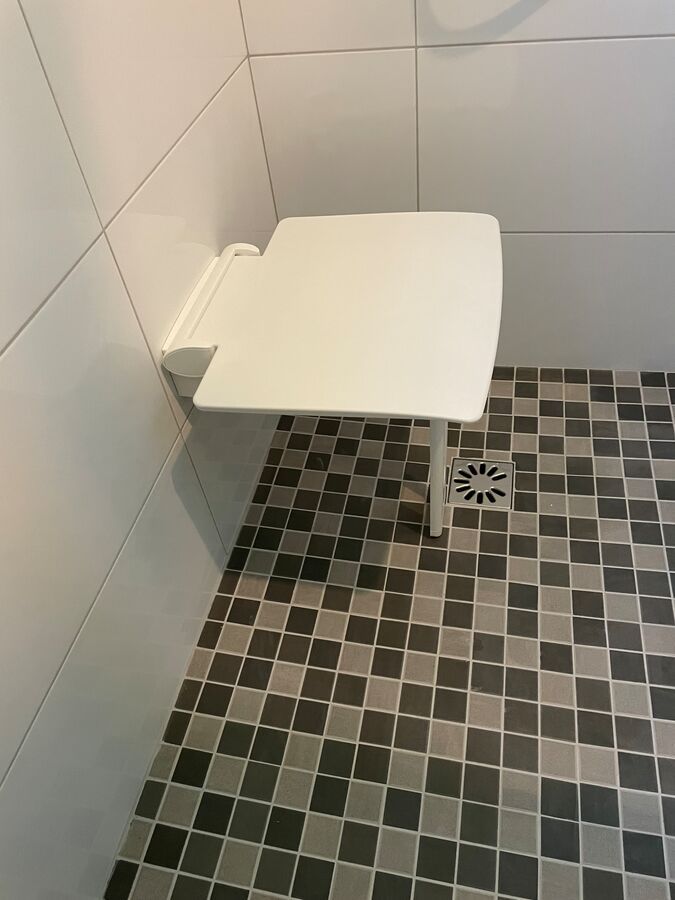 Un siège de douche est posé sur un sol carrelé dans une salle de bain.