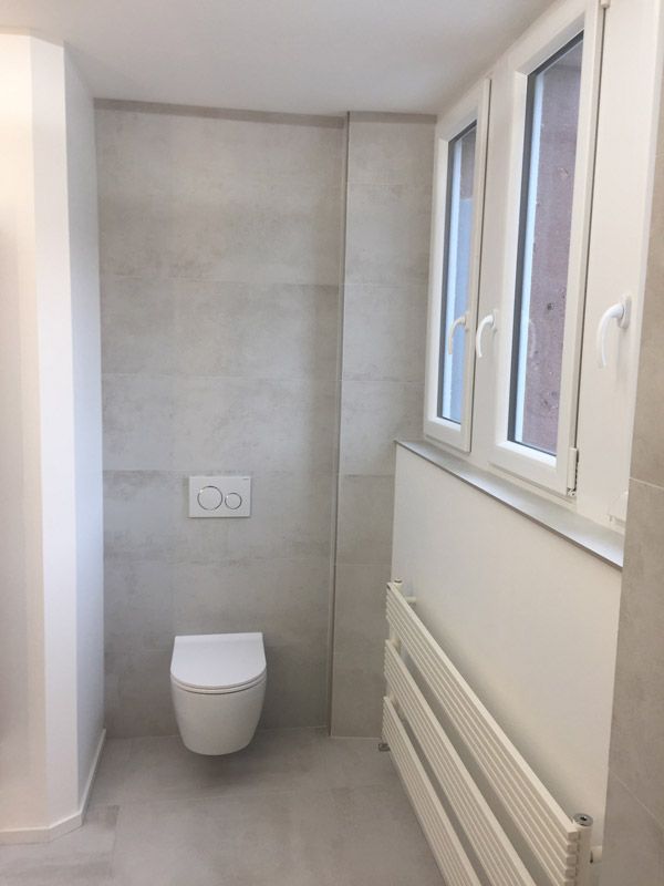 Une salle de bain avec WC et deux fenêtres.