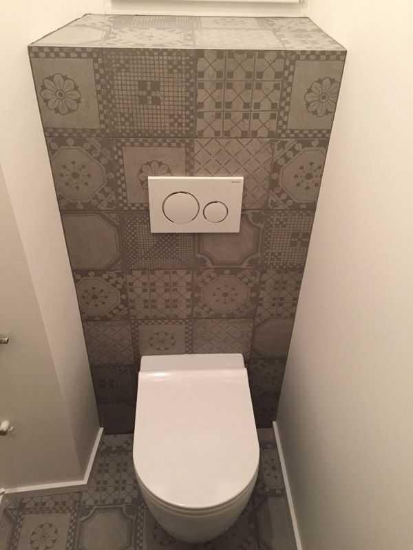 Des toilettes dans une salle de bain avec un mur carrelé derrière.