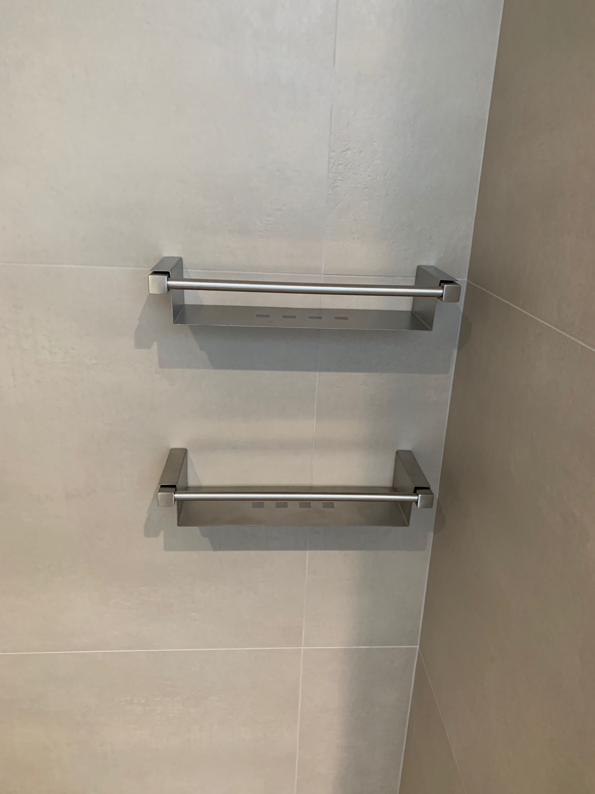 Deux porte-serviettes en acier inoxydable sont accrochés sur un mur carrelé dans une salle de bain.