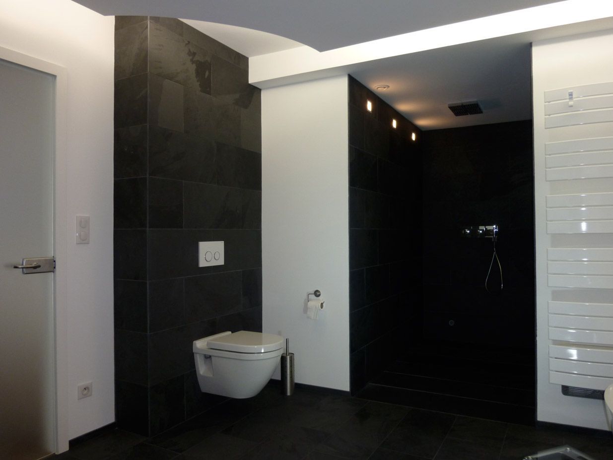 Salle de bain moderne avec des touches de carrelage noir, des toilettes murales et une douche aux parois de verre.