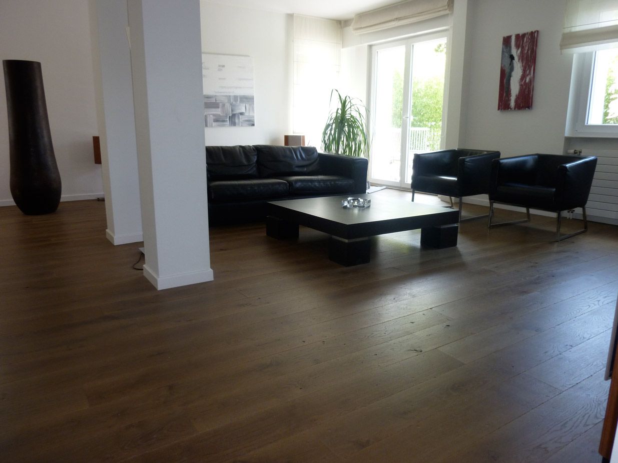 Salon avec parquet en bois foncé, meubles en cuir noir et colonnes blanches.