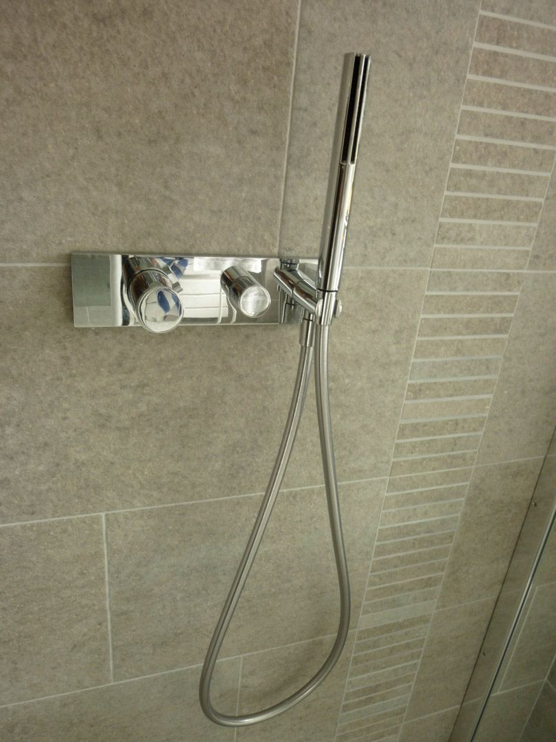 Une pomme de douche avec un tuyau attaché est accrochée à un mur carrelé.