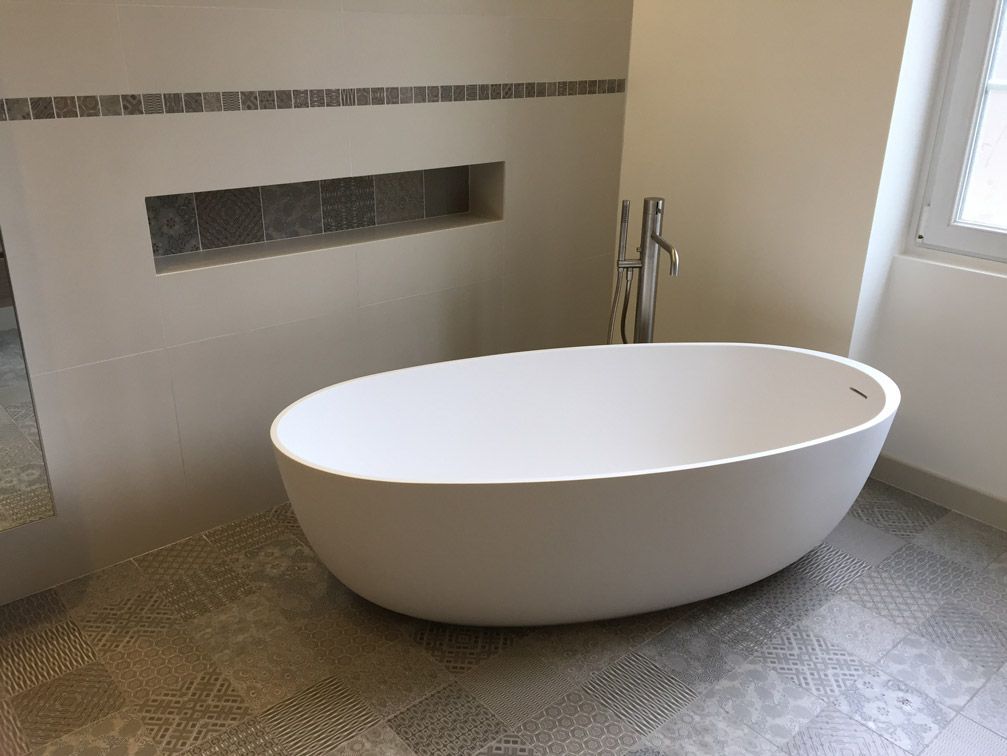 Une baignoire blanche se trouve dans une salle de bain à côté d'une fenêtre.