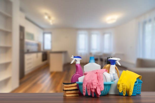 Cleaning supplies: spray bottles, gloves, sponges, in front of a blurred living area.