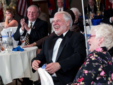 A man in a tuxedo is laughing while sitting at a table with other people