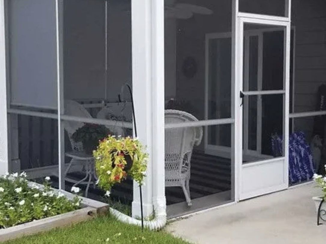 A screened in porch with a wicker chair , table and chairs.