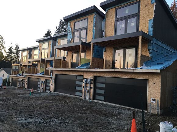 Row of modern townhouses under construction, with black garage doors, large windows, and unfinished siding.