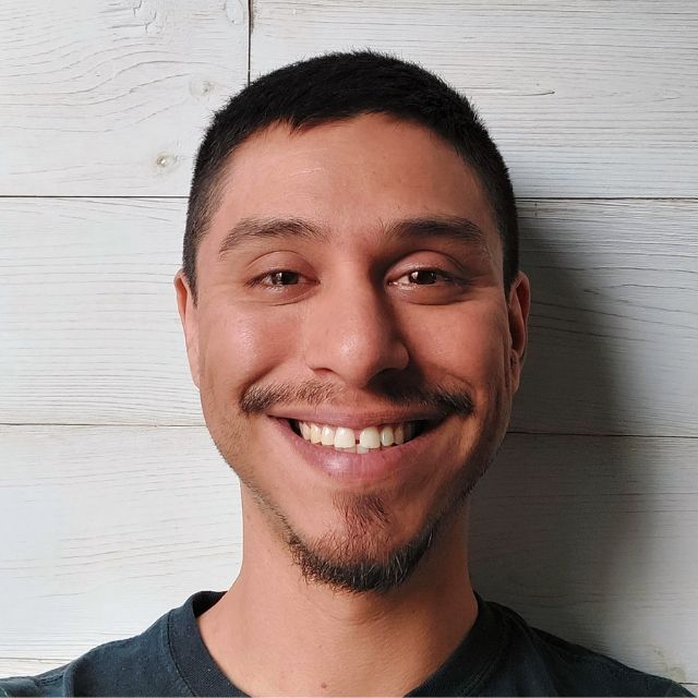 A man with a beard is smiling in front of a white wall