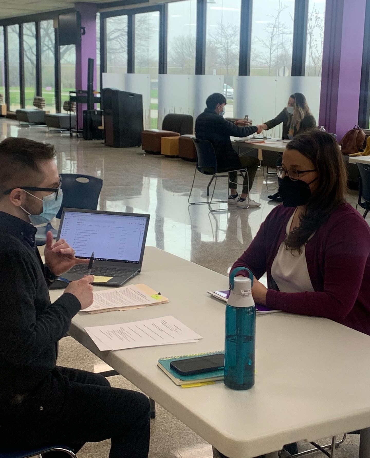 A man and a woman are sitting at a table with a laptop and a water bottle.